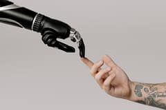 team-01 A human hand with tattoos reaching out to a robotic hand on a white background.