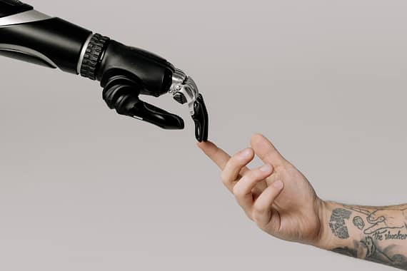 services-01 A human hand with tattoos reaching out to a robotic hand on a white background.